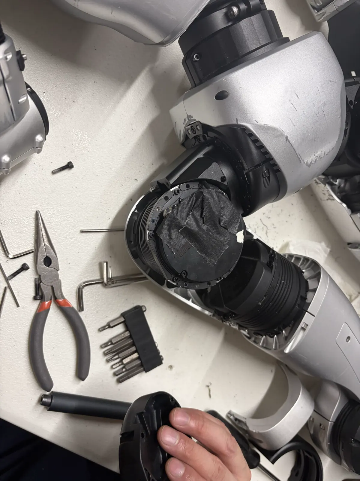 Workbench with hex keys, pliers, a bit set, and the opened hip actuator